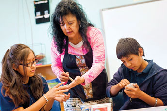 Noreen Simplicio helps 6th-graders Lori Yukestine, left, and Kynan Sanchez with their work during a traditional pottery making workshop at Zuni Middle School Tuesday. © 2011 Gallup Independent / Cable Hoover 